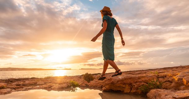 Mujer paseando en Ibiza con puesta de sol y mar